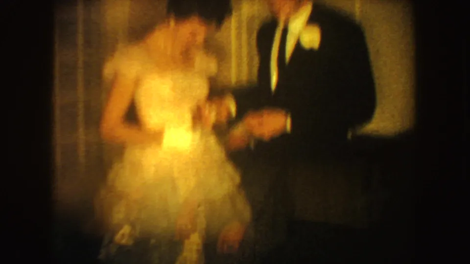 A soft, motion-blurred 1954 South Dakota frame shows the formal couple shifting position in warm interior light.