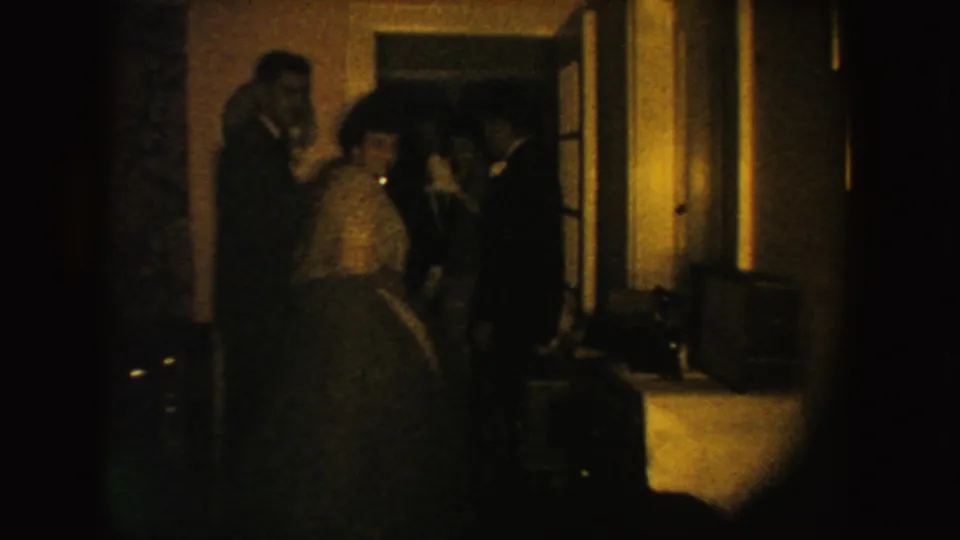 Several adults in formal clothing cluster by a doorway in warm, grainy 1954 South Dakota home-movie footage.