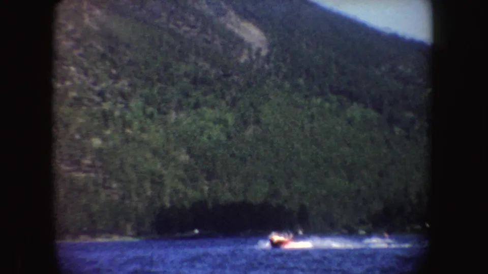 1954 South Dakota home-movie view of a small speedboat cutting across lake water beneath dense green hillsides.