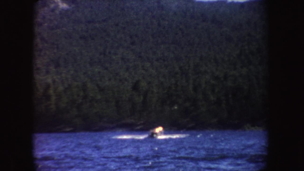 A distant speedboat throws a white wake across a blue lake, backed by dark forested hills in South Dakota.