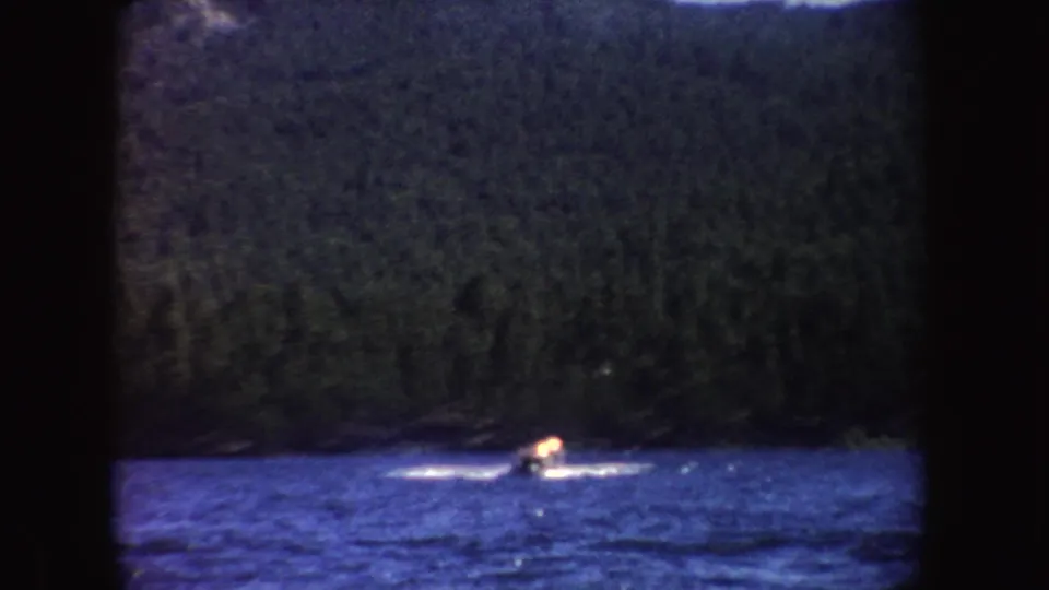 A distant speedboat throws a white wake across a blue lake, backed by dark forested hills in South Dakota.