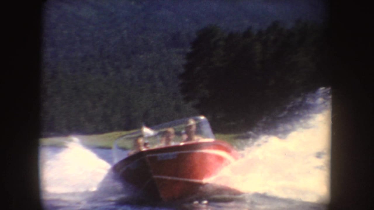 A red open motorboat speeds across a South Dakota lake with passengers visible behind the windshield and spray rising around the hull.