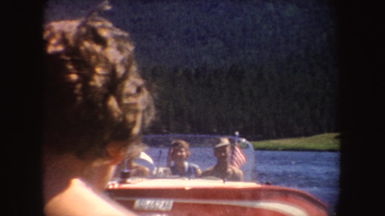 A person’s curly hair fills the foreground as a red motorboat with visible passengers moves across a South Dakota lake behind them.