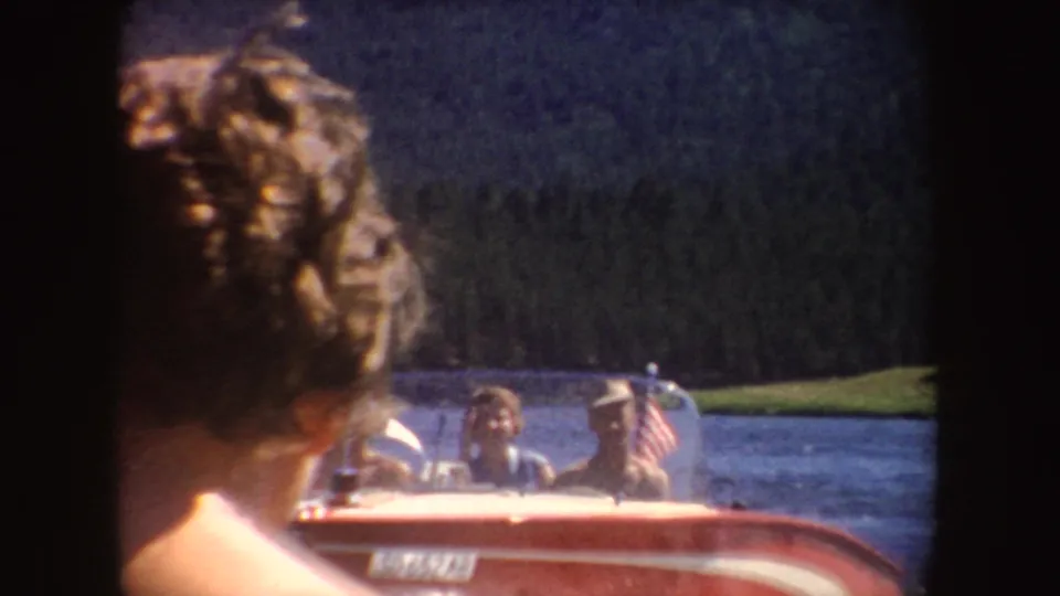 A person’s curly hair fills the foreground as a red motorboat with visible passengers moves across a South Dakota lake behind them.