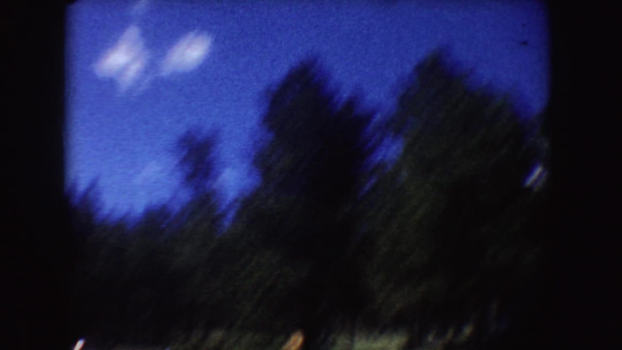 Blurred shoreline trees and blue sky seen through a dark 8mm film frame border.