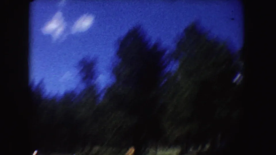 Soft, blurred 8mm view of shoreline greenery and blue sky, likely from the same South Dakota lake sequence.
