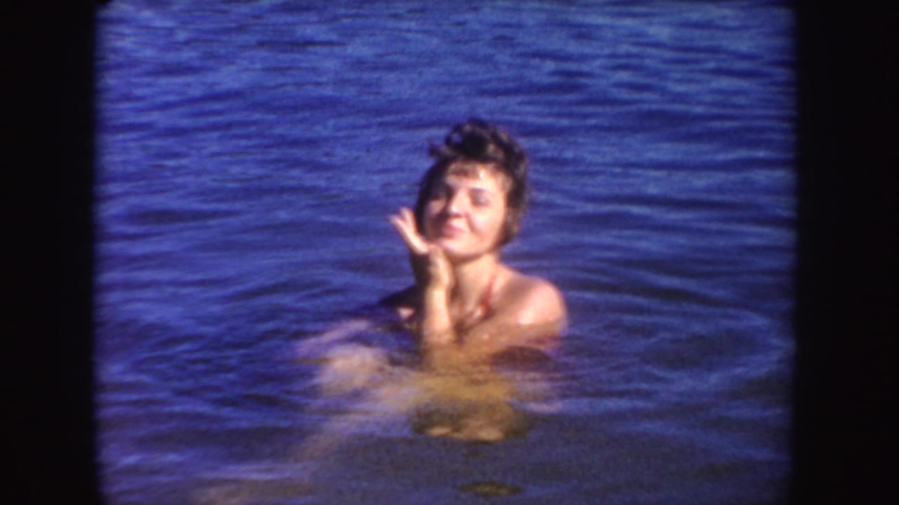 Woman swimming in a South Dakota lake in 1954, smiling toward the camera with rippling blue water around her.
