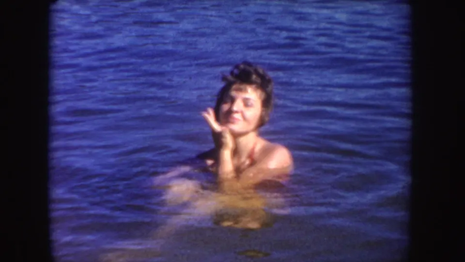 Woman swimming in a South Dakota lake in 1954, smiling toward the camera with rippling blue water around her.