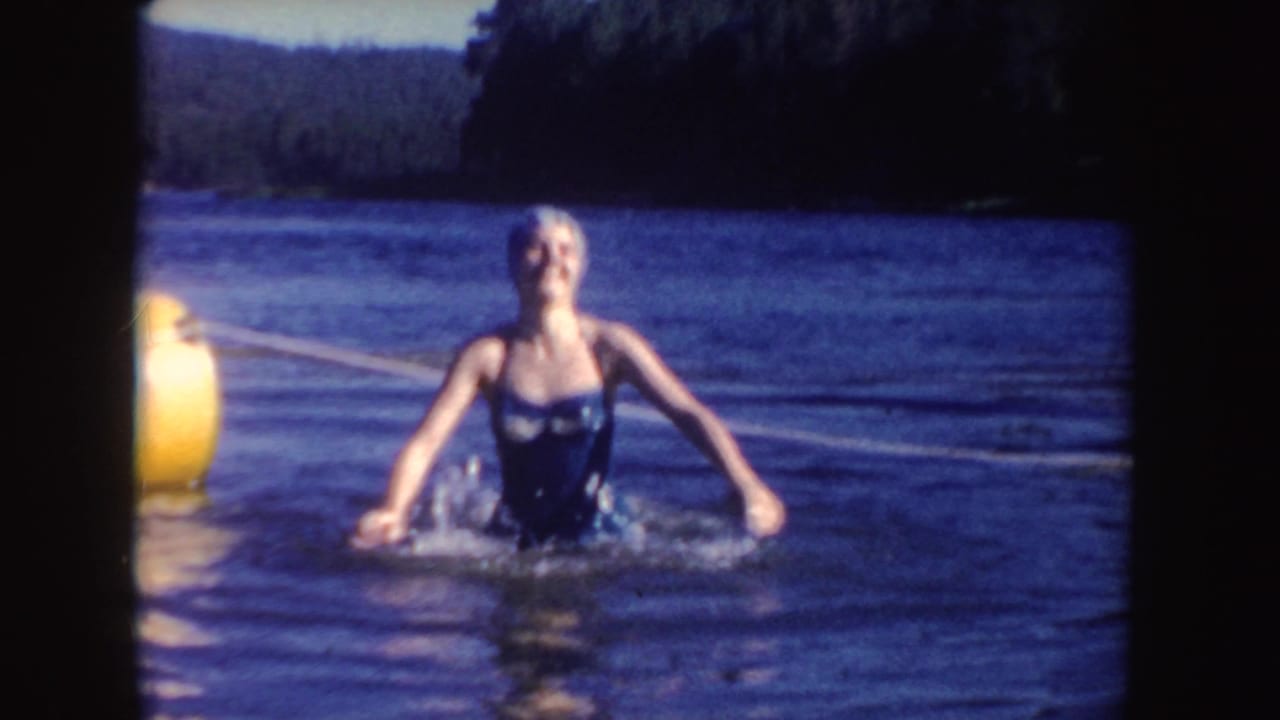 In South Dakota 1954 home-movie footage, an adult woman in vintage swimwear moves through the lake near a yellow buoy.