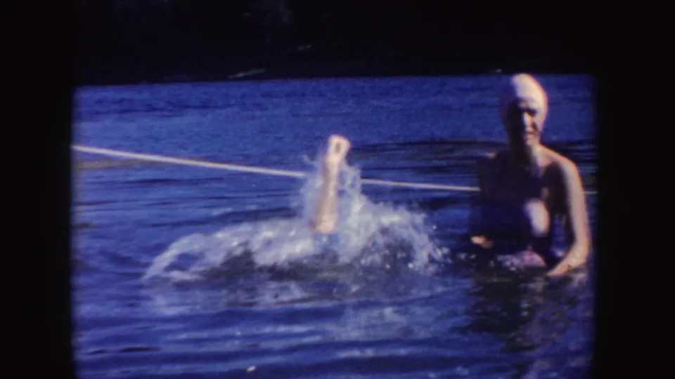 In South Dakota home-movie footage from 1954, two women in swim caps and bathing suits play in a lake while water splashes in front of them.