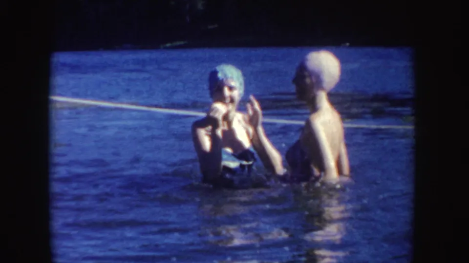 Two adult women in swim caps and swimsuits stand in South Dakota lake water, one facing the camera while the other turns sideways.