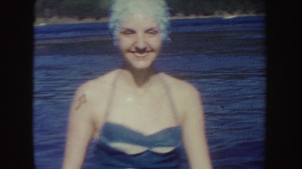 Smiling adult woman in a pale swim cap and dark strapless swimsuit faces the camera while standing in a South Dakota lake.