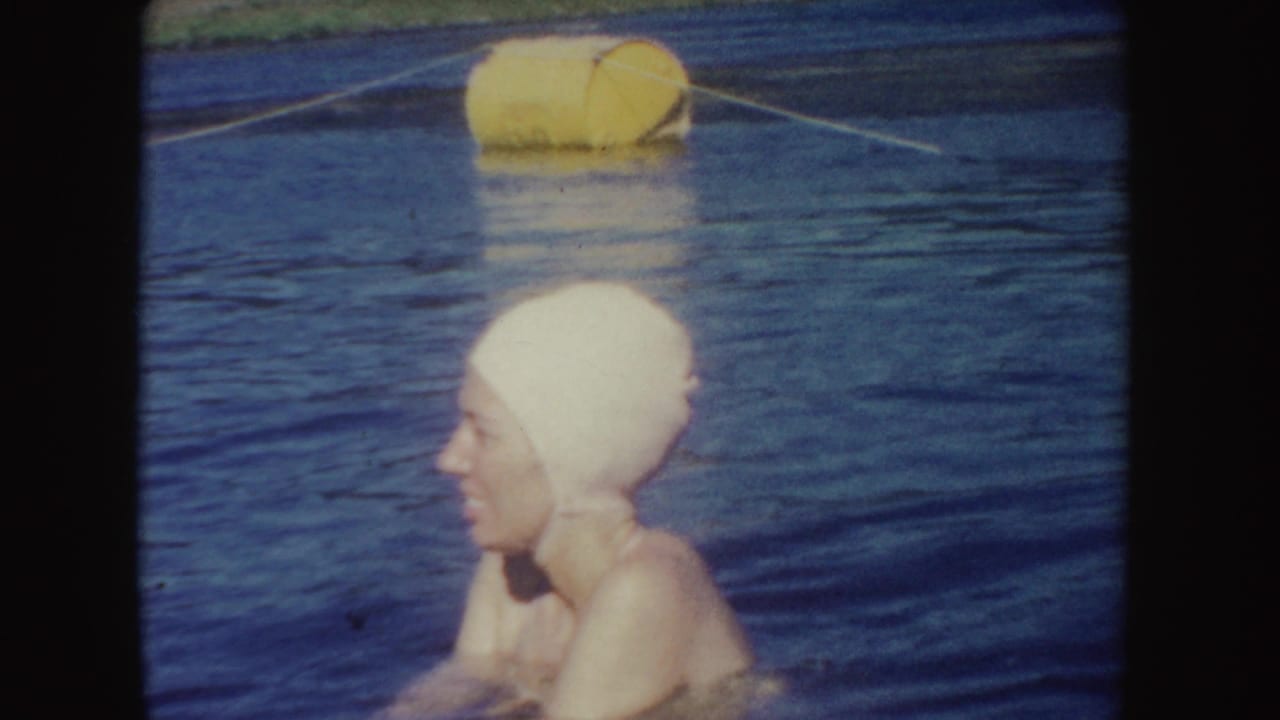 Adult woman in profile, wearing a light swim cap, stands in lake water below a yellow buoy and rope line in South Dakota.