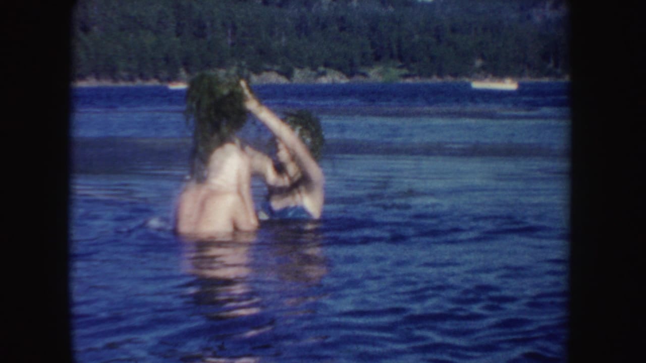 One swimmer lifts wet hair while another reaches toward it in the lake.