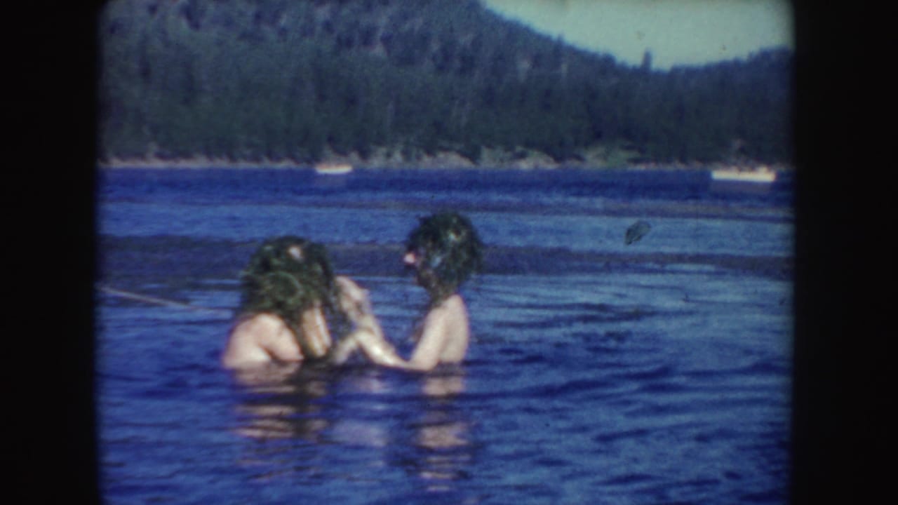 1954 South Dakota home-movie frame showing two young women laughing and adjusting wet hair in a lake.
