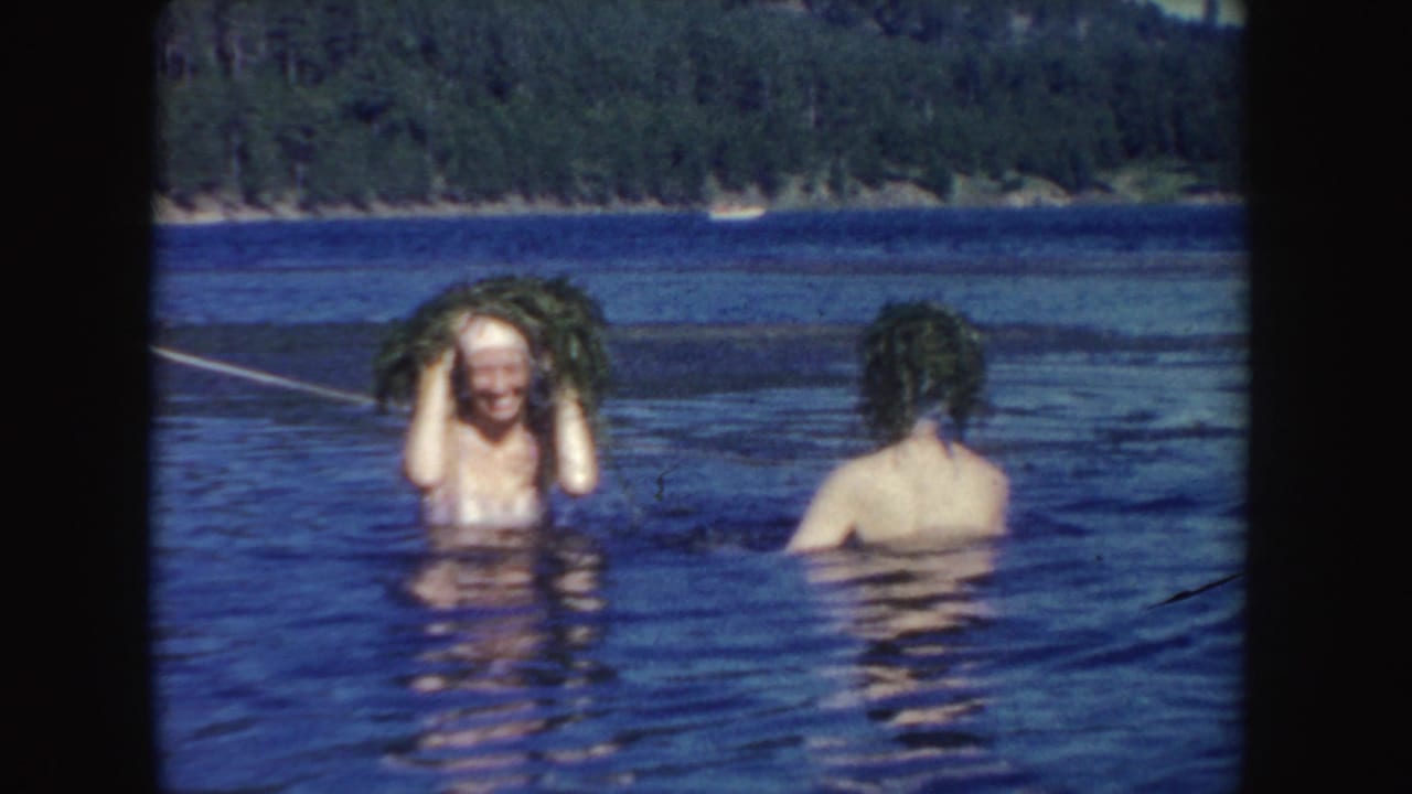 1954 South Dakota 8mm frame with one young woman smiling under lifted wet hair as another swimmer faces away.