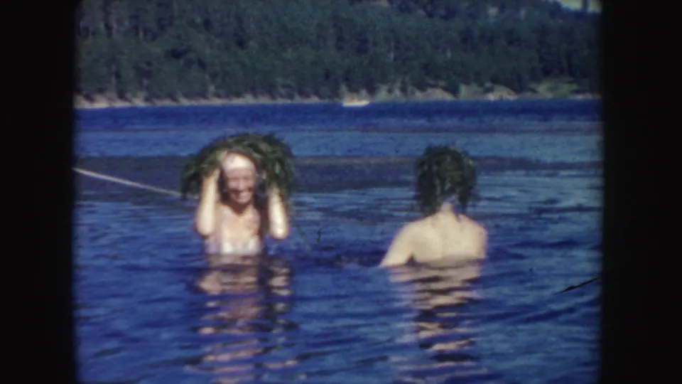 1954 South Dakota 8mm frame with one young woman smiling under lifted wet hair as another swimmer faces away.