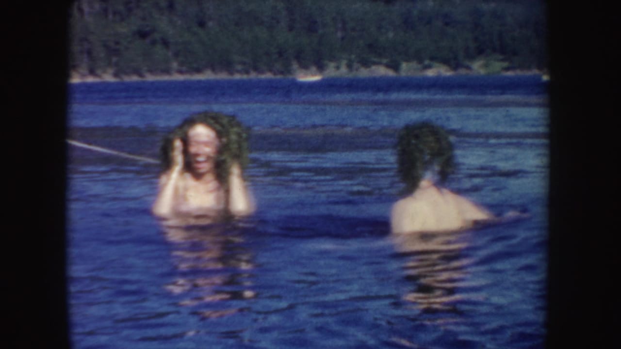 In 1954 South Dakota home-movie footage, two women are chest-deep in a lake as one laughs toward the camera with wet hair.