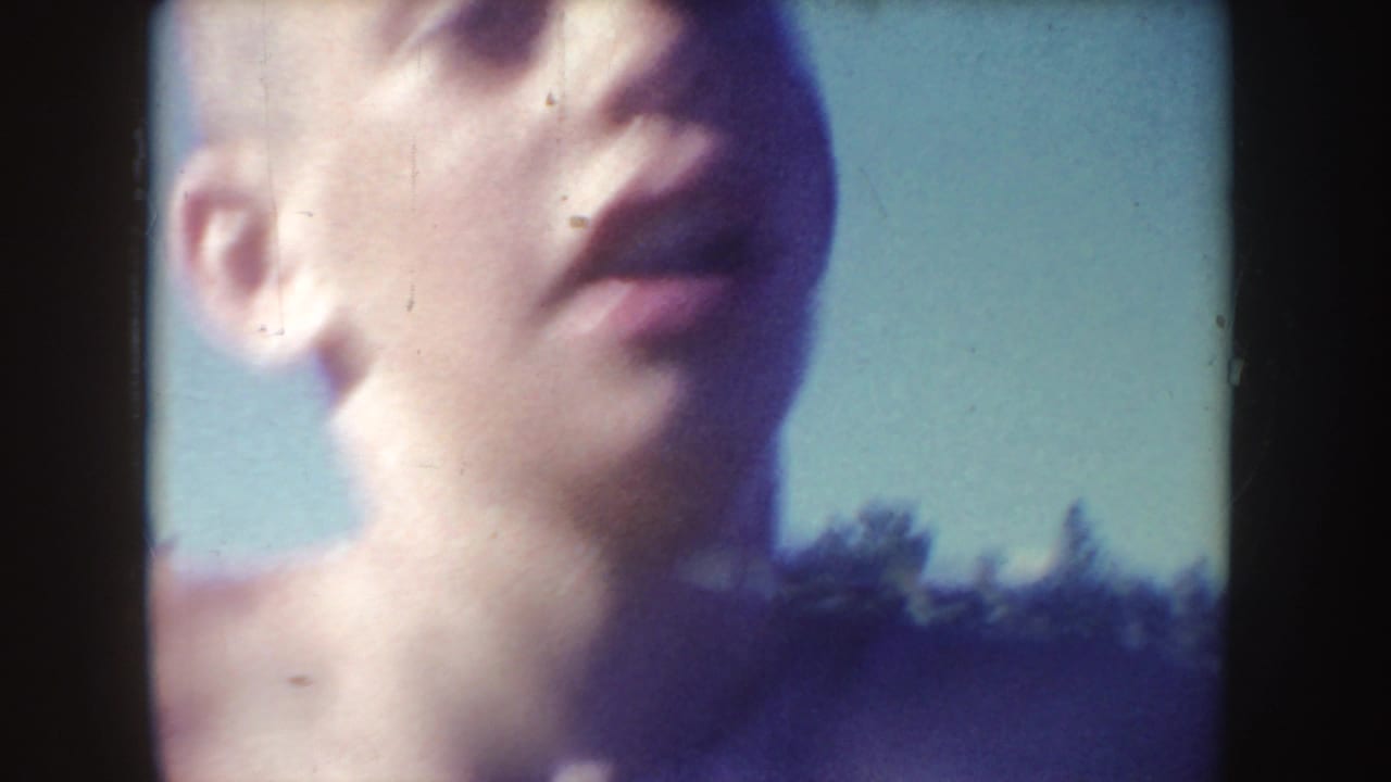 Close upward view of a swimmer's face against blue sky and shoreline.