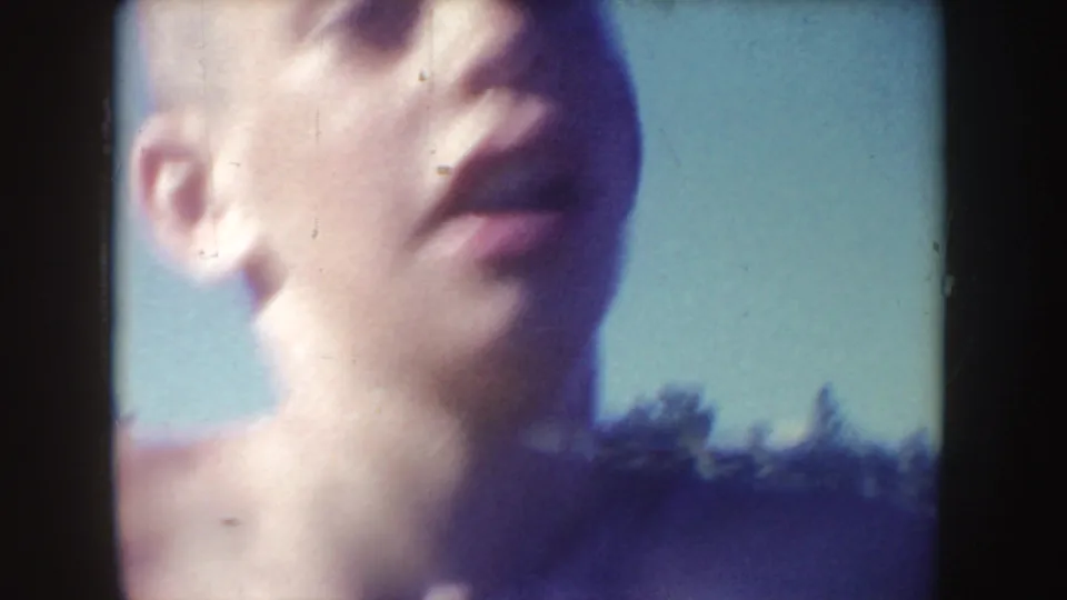 Close 8mm view of a swimmer's face above the water, with blue sky and a dark shoreline behind.