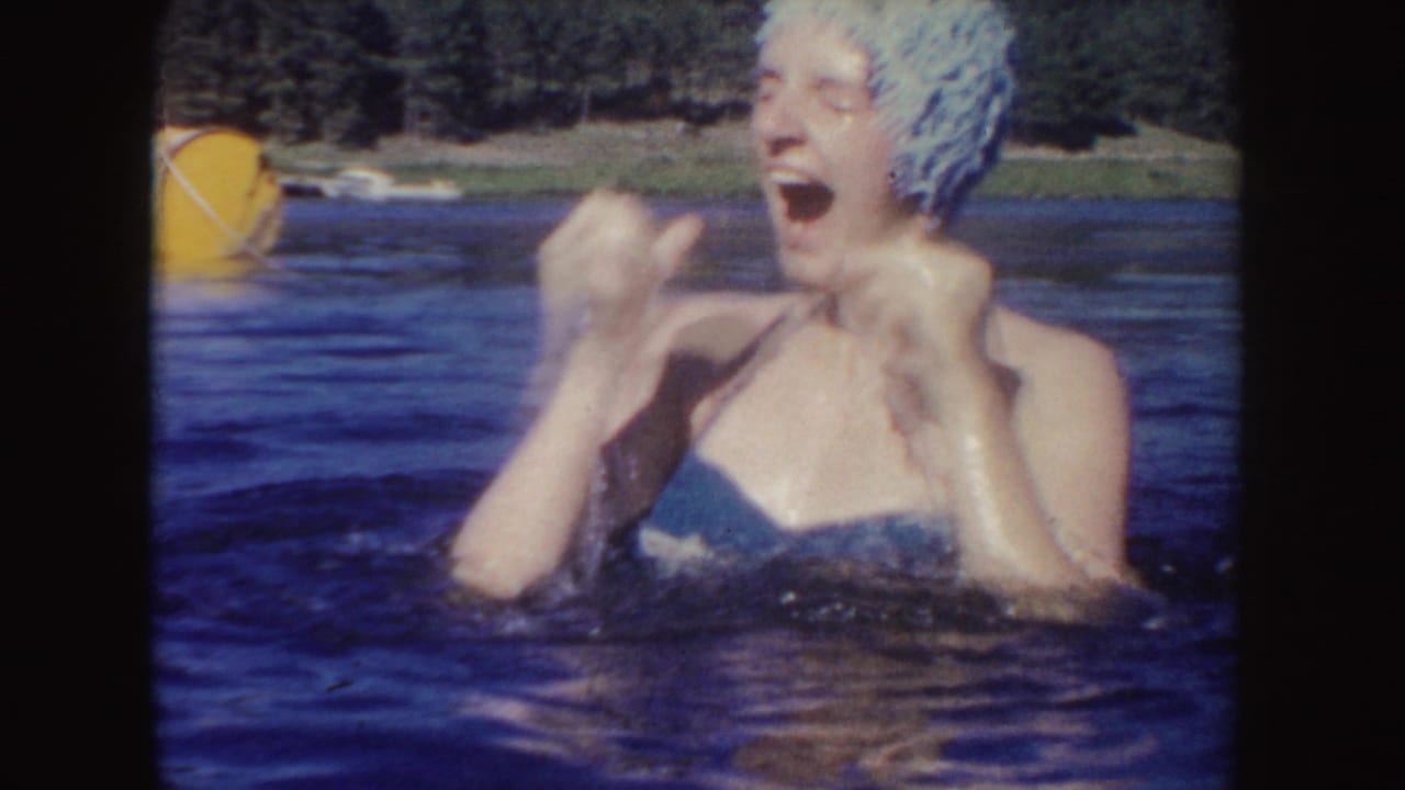 1954 South Dakota home-movie frame of a swimmer in a light swim cap laughing and splashing in the lake.