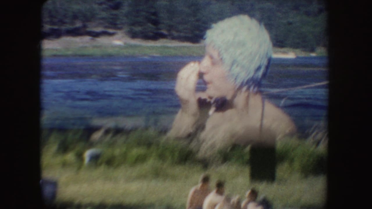 Woman in a light swim cap laughs in lake water with swimmers along the shore below.
