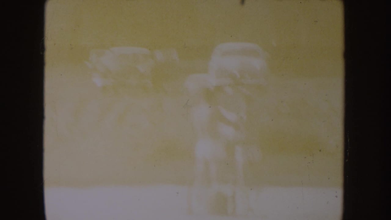 Faded 1954 South Dakota lake footage with two barely defined figures standing near the shore in heavy overexposure.