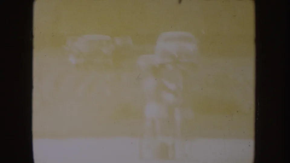 Faded 1954 South Dakota lake footage with two barely defined figures standing near the shore in heavy overexposure.