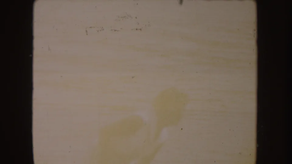 Faded 8mm frame from the South Dakota home movie, with faint adult figures barely visible against a washed, warm-toned scene.