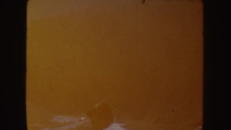 Warm, underexposed 8mm frame from the river play scene, with a blurred adult figure near the lower edge and heavy color shift.
