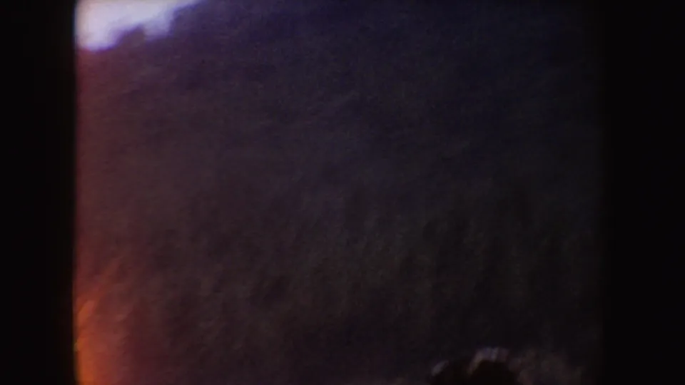 Dark, motion-blurred 8mm frame from the 1954 South Dakota clip, with a partial indistinct figure and warm edge flare.