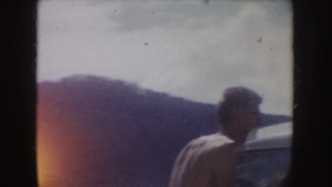 1954 South Dakota frame of a man beside a parked car, silhouetted against hazy hills and a bright sky.