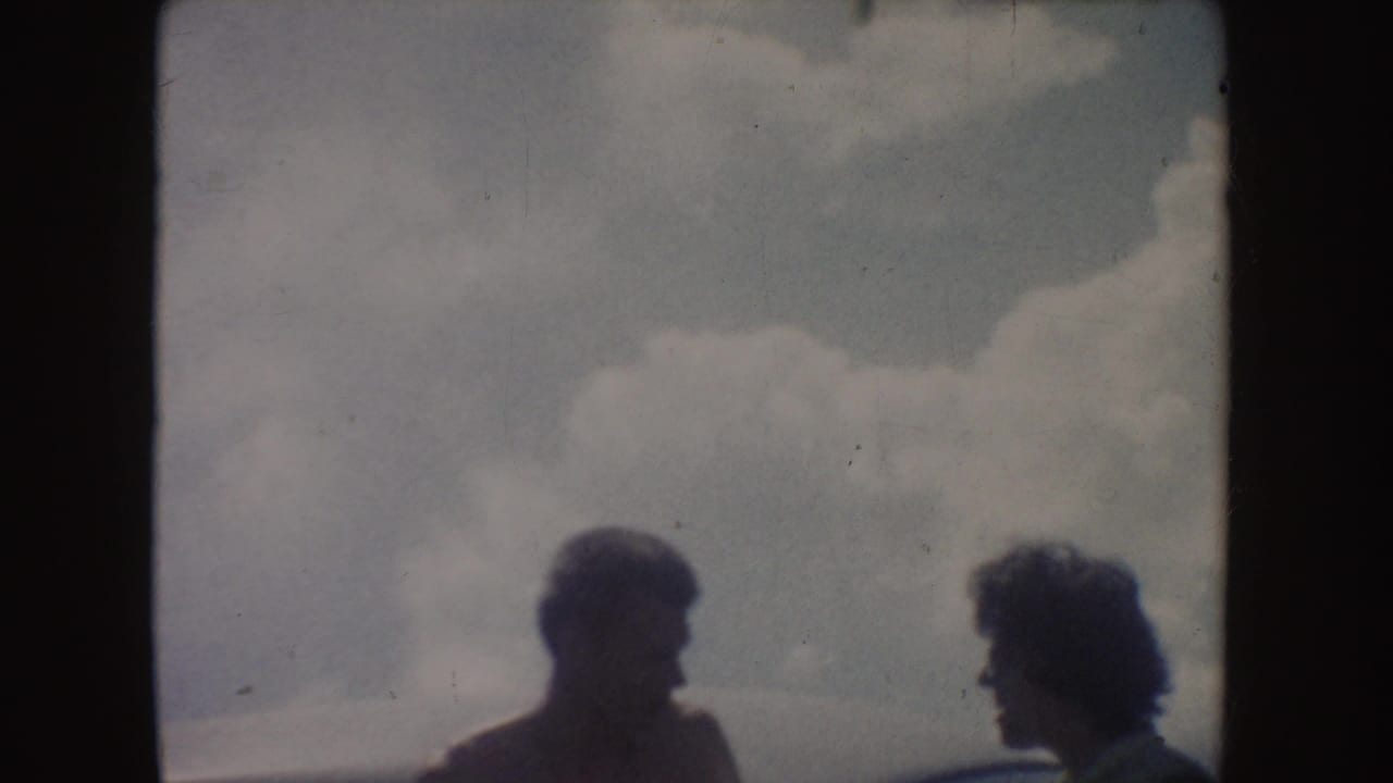 Soft 8mm frame showing two people in side profile beneath large clouds, with facial detail obscured by backlighting.