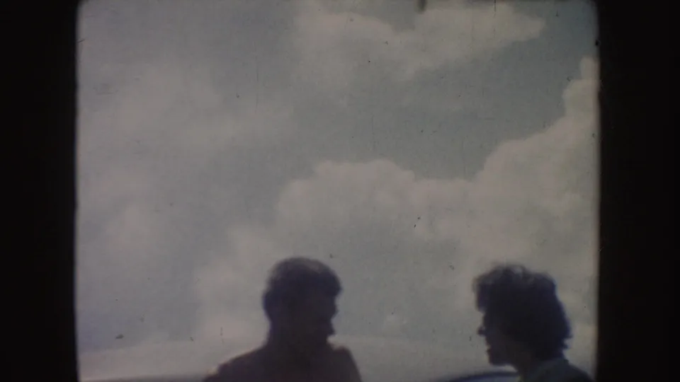 Soft 8mm frame showing two people in side profile beneath large clouds, with facial detail obscured by backlighting.