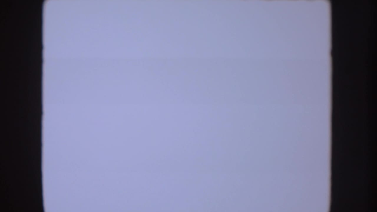 Overexposed 8mm frame with pale blue-white field and dark film edges, likely part of the same 1954 South Dakota home-movie clip.