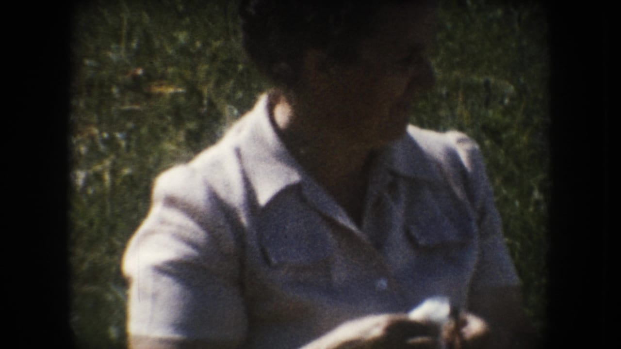Woman in a light collared dress and glasses holds a small white object outdoors in South Dakota home-movie footage from 1954.