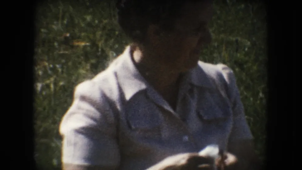 Woman in a light collared dress and glasses holds a small white object outdoors in South Dakota home-movie footage from 1954.