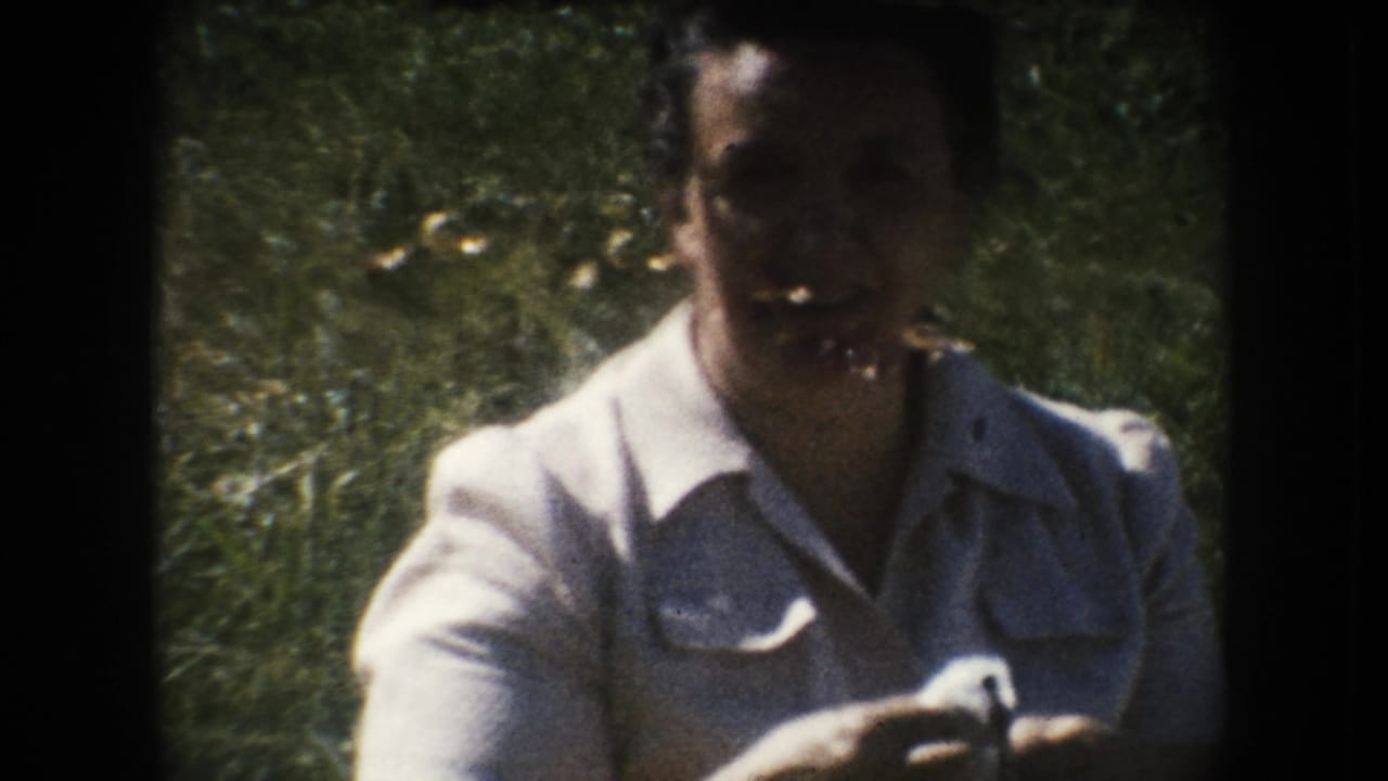 Smiling woman in a light collared dress stands outdoors with greenery behind her in 1954 South Dakota 8mm home-movie footage.