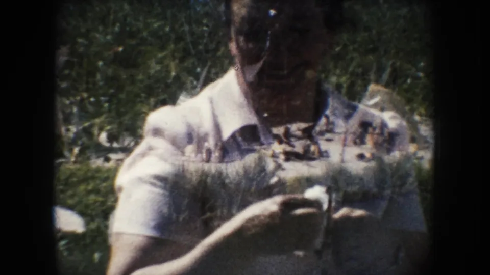 Woman in glasses and a light dress holds a small white object outdoors, with 8mm grain, foliage, and exposure overlap visible.