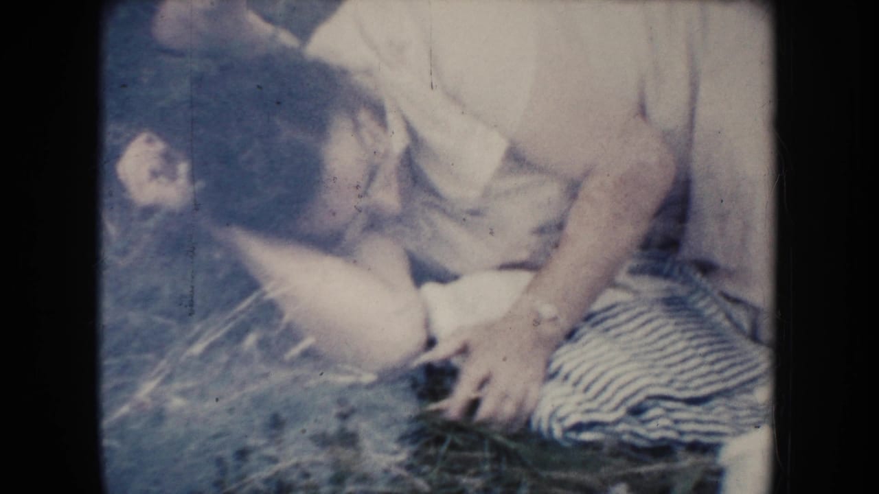 A woman in a light short-sleeved shirt reclines beside the patterned blanket in the 1954 South Dakota yard footage.