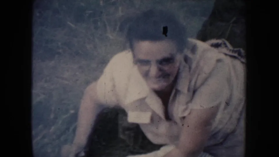 The woman sits up on the grass and smiles toward the camera in this 1954 South Dakota 8mm home-movie frame.