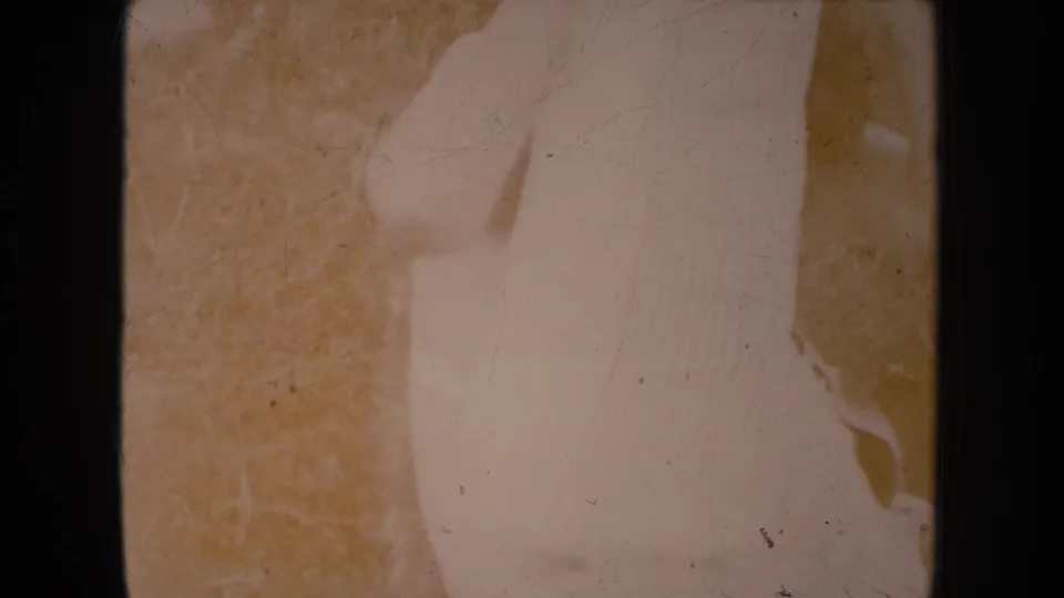 A faded, overexposed 8mm frame shows pale fabric or dress material with grass at the edge.