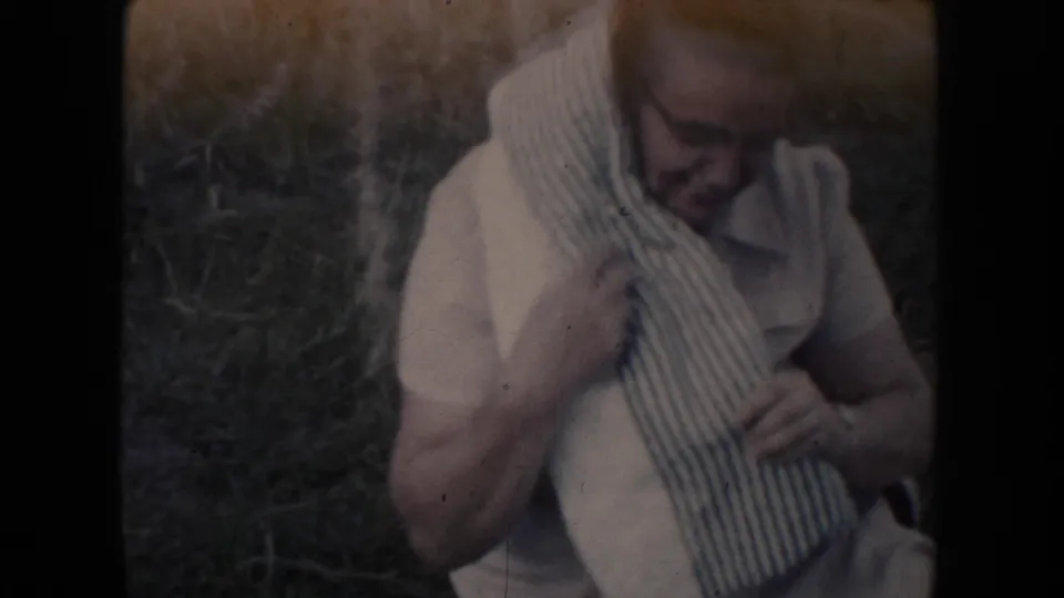 The woman smiles slightly while holding a striped checked cloth against her white dress outdoors.