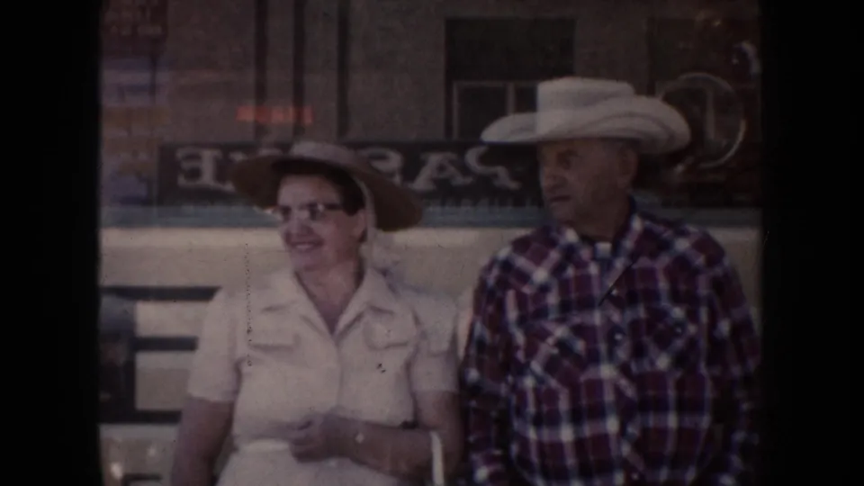 South Dakota 1954 home-movie frame showing a smiling woman and a man in cowboy hats beside a building with partial signage.