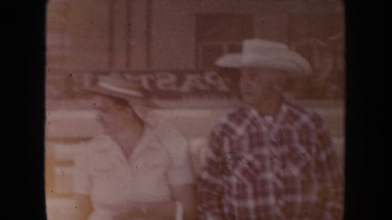 Older couple in cowboy hats stands in soft double exposure near a storefront.