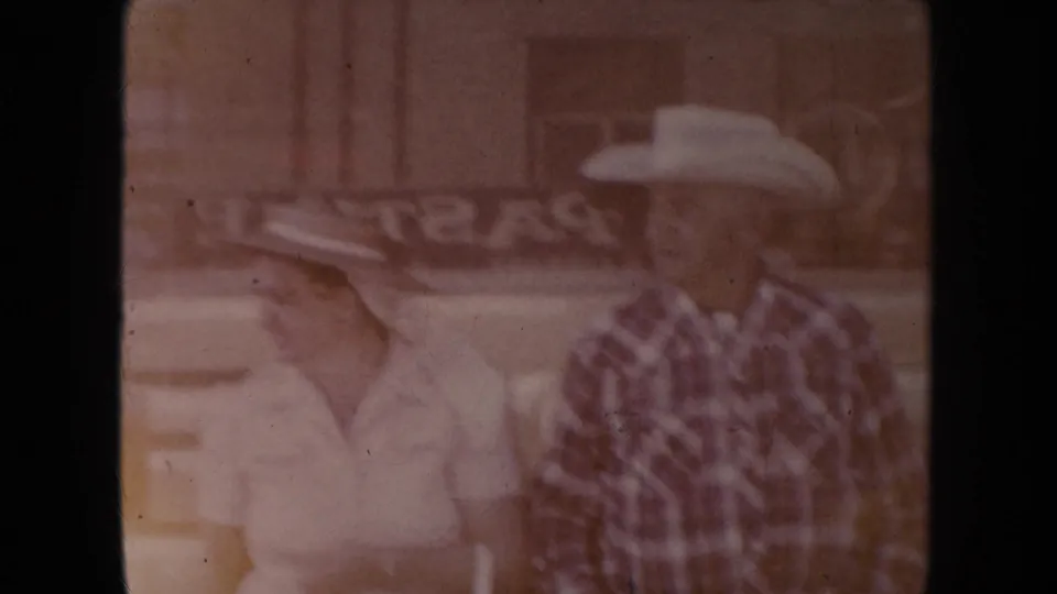 In 1954 South Dakota footage, an older couple in cowboy hats appears faintly over a storefront scene due to double exposure.