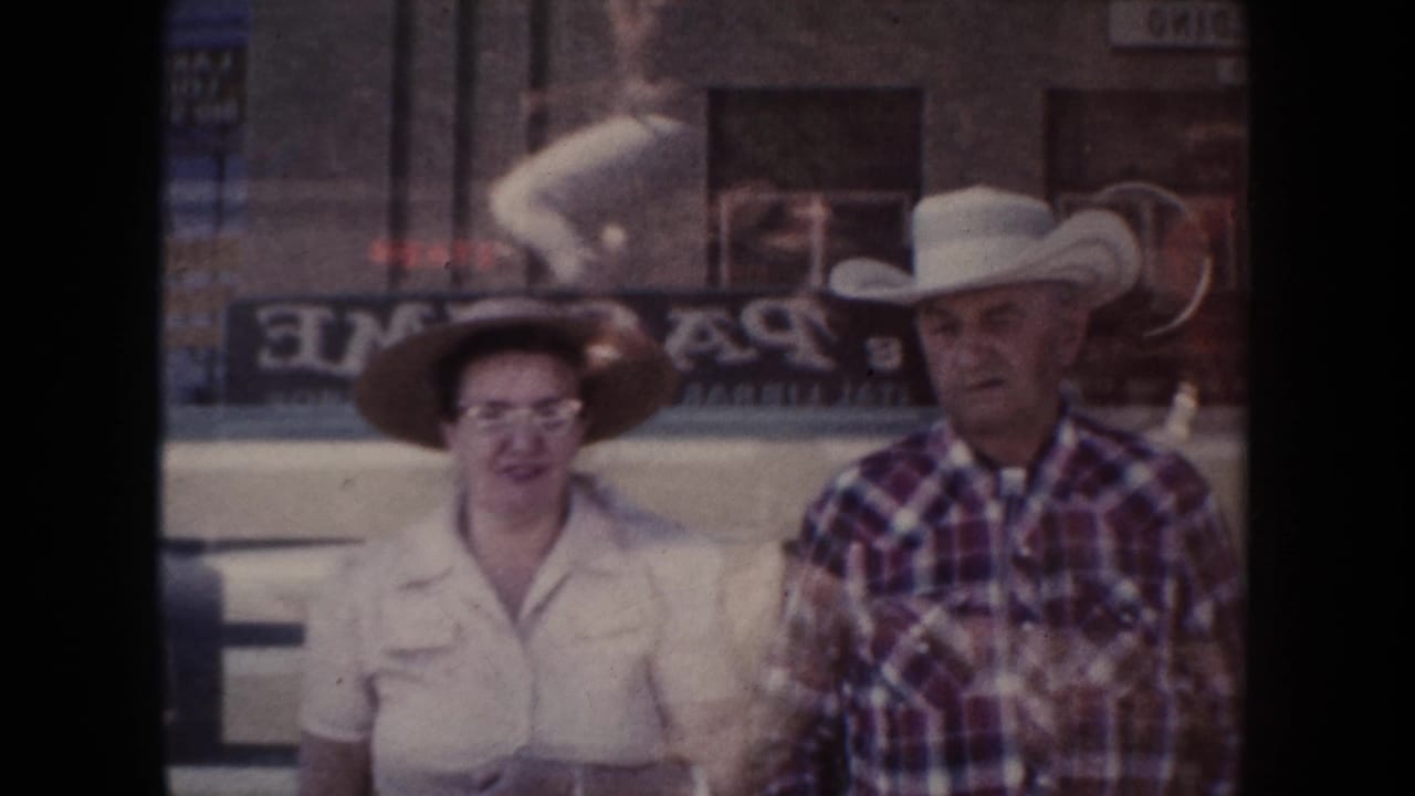 Older woman and man in Western-style hats stand in front of storefront windows.
