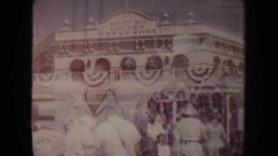 The Golden Horseshoe building appears with patriotic bunting, while faint overlaid figures show the home-movie double exposure.