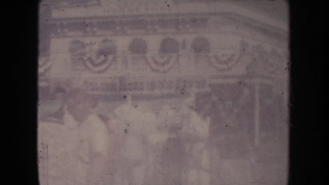 Faded view of people near a building decorated with bunting.