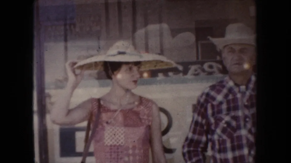 1954 South Dakota frame showing a woman in a wide straw hat and a man in a cowboy hat standing outdoors.